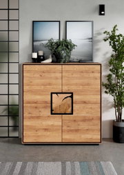 Frontale Ansicht einer modernen Holz-Kommode/Sideboard in Eiche-Optik mit schwarzem Rahmen und quadrativem Griffdetail, dekoriert mit Pflanzen, Kerzen und gerahmten Bildern im Wohnraum.