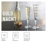 Twee elegante champagneglazen met gouden versieringen, het ene met een geometrisch patroon en het andere met notenbalken, op een tafel naast een fles mousserende wijn, gezien vanuit een zijdelingse hoek.