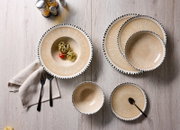 Van bovenaf gefotografeerd beige servies met een verfijnd straalpatroon en zwart gestippelde rand, stijlvol gedekt met pasta, zwart bestek en een linnen servet op een lichte houten tafel.