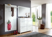 Moderne garderobecombinatie met een witte schoenenkast in hoogglans, een grote spiegel en een garderobepaneel met haken en een legplank, gezien vanaf de zijkant.