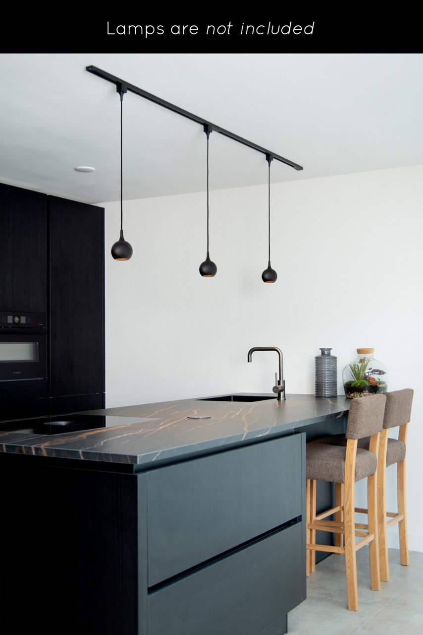 Moderne Küche mit schwarzem Schienensystem an der Decke, an dem drei Pendelleuchten hängen. Perspektive von der Seite der Kücheninsel.