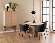 Moderner Esstisch aus Holz mit runder Tischplatte und vertikalen Streben, umgeben von vier dunkelgrauen Stühlen, in einem stilvoll eingerichteten Raum mit Holzschrank und Pflanzen, seitliche Perspektive.
