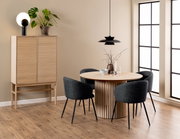 Moderner Esstisch aus Holz mit runder Tischplatte und vertikalen Streben, umgeben von vier dunkelgrauen Stühlen, in einem stilvoll eingerichteten Raum mit Holzschrank und Pflanzen, seitliche Perspektive.