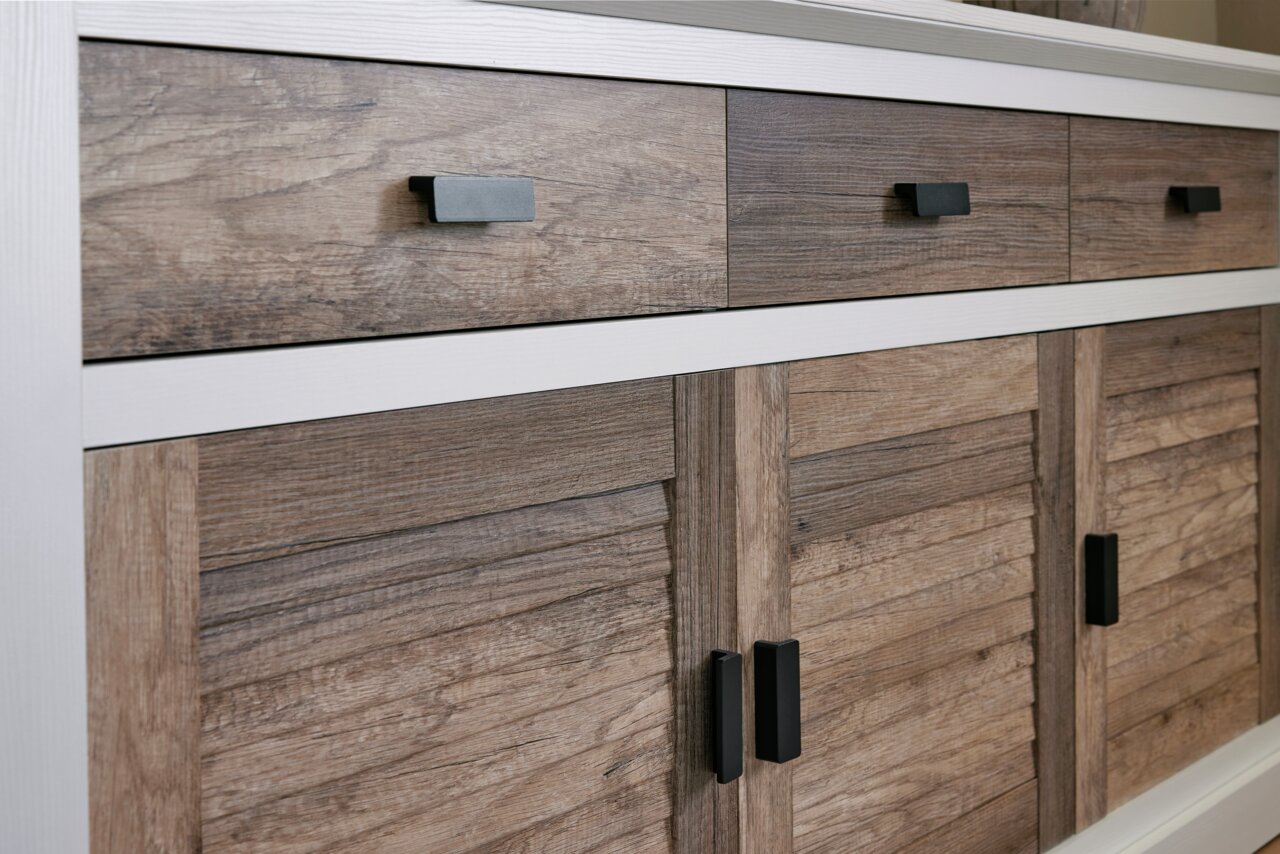 Close-up van een dressoir met houtlook en zwarte handgrepen, gezien van voren.