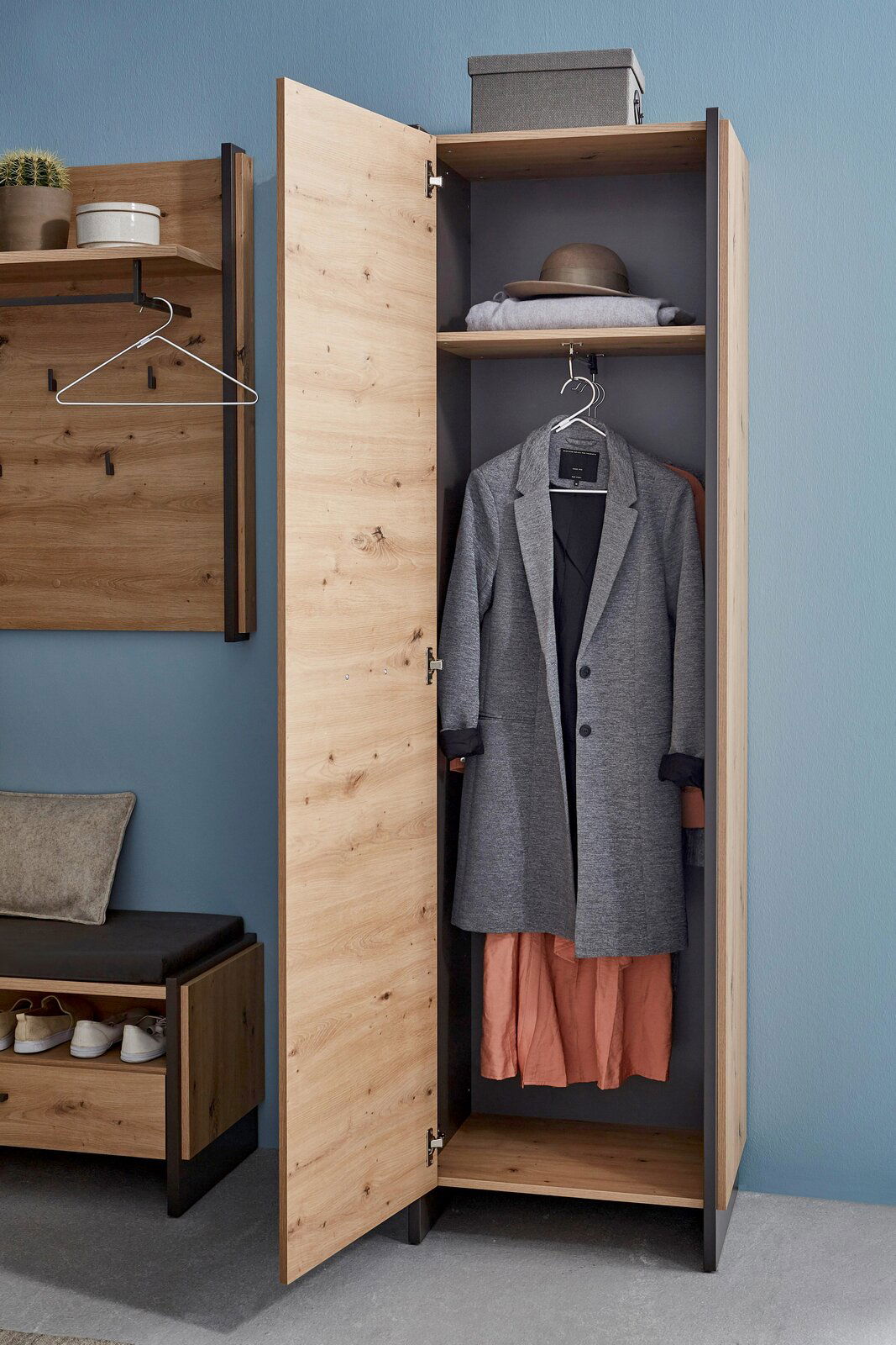 Garderobenschrank aus Holz mit geöffneter Tür, zeigt Innenraum mit Kleiderstange, Mantel und Hut, seitliche Perspektive