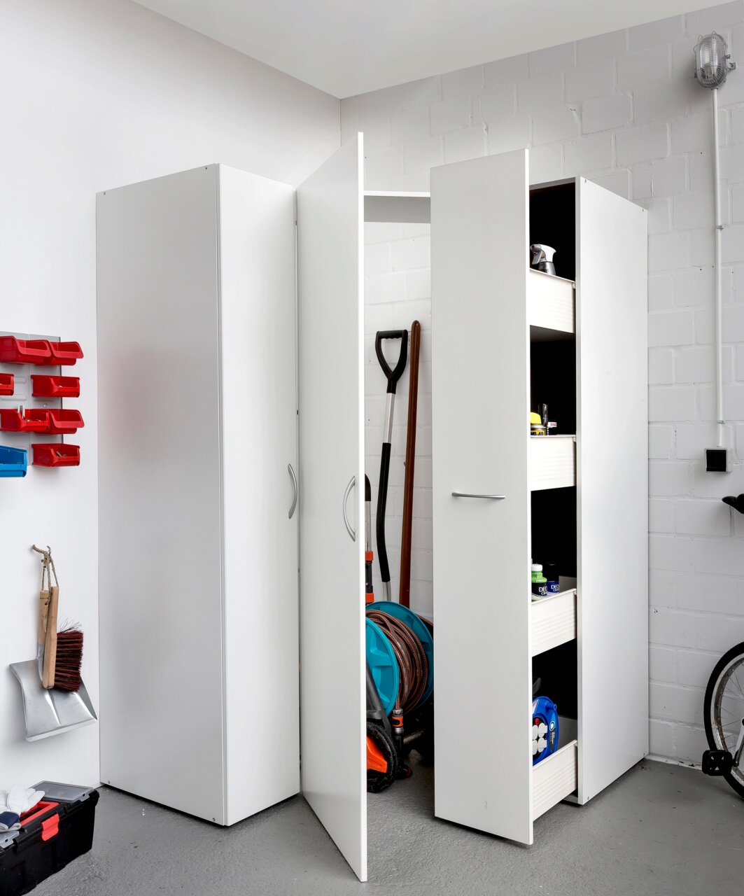 XORA Apothekerschrank MULTIRAUMKONZEPT Mehrzweckschrank in einer Garage, teilweise geöffnet, mit Blick auf Regale und gelagerte Gegenstände.