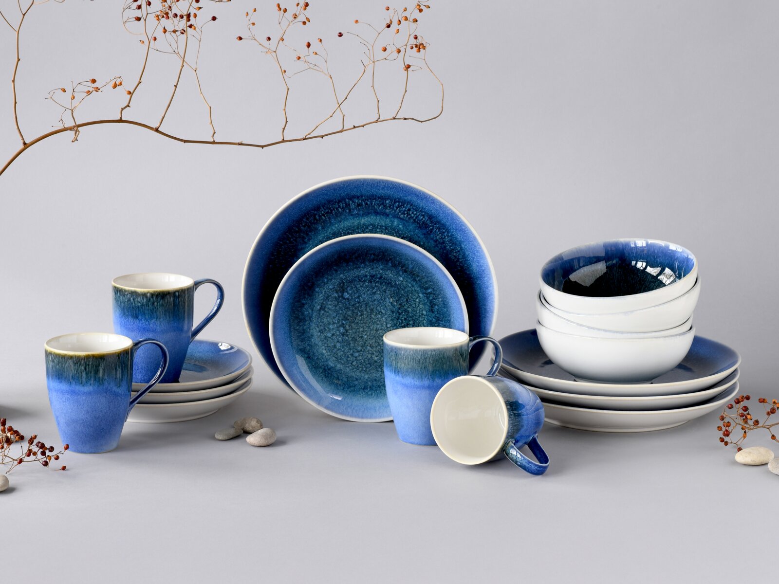 Creatable Kombiservice 16-tlg CALDERA Blau glasiertes Keramik-Geschirrset mit Tellern, Schalen und Tassen auf grauem Hintergrund, frontal in leichter Schrägansicht arrangiert
