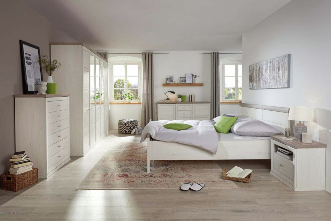 Helles Schlafzimmer mit einem Bett 140x200 in der Mitte, umgeben von weißen Möbeln und dekorativen Elementen, aus der Perspektive von der Zimmertür aus gesehen.