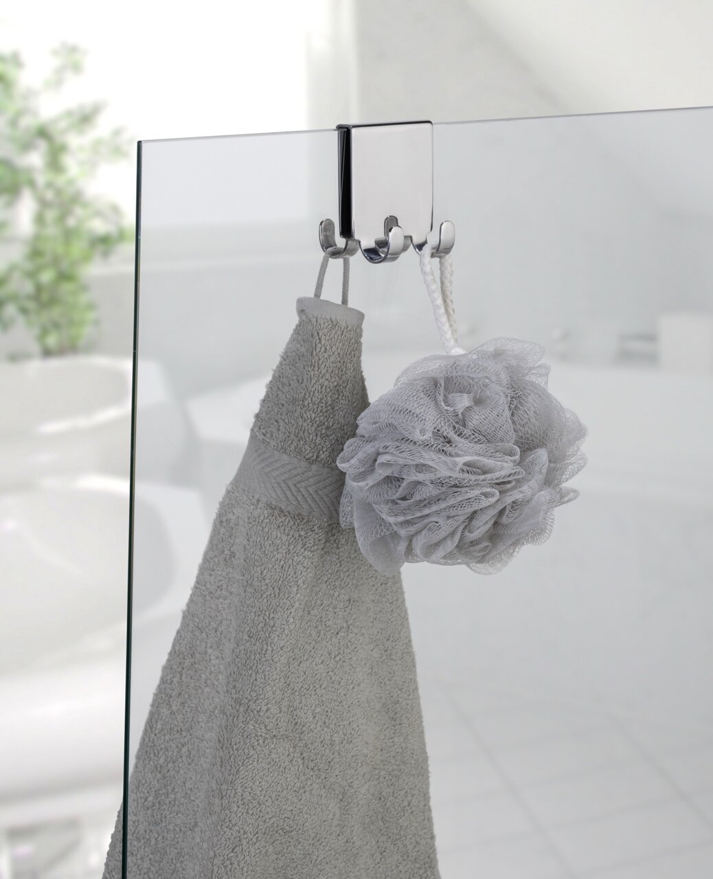 Edelstahl Doppel-Duschhaken an einer Glastür, von vorne betrachtet, mit einem Handtuch und einem Duschschwamm aufgehängt.