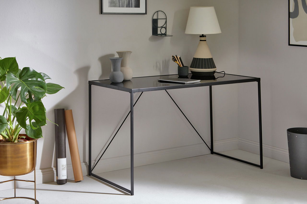 Jahnke Schreibtisch GLAM Moderner Schreibtisch mit schwarzer Glasplatte und schlankem Metallgestell, seitliche Perspektive, dekoriert mit Vasen, Lampe und Pflanzen.