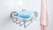 Nahaufnahme eines verchromten Seifenkorbs von tesa Aluxx mit blauer Seife, montiert an einer weißen Badezimmerwand.