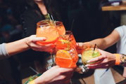 Meerdere mensen proosten met kleurrijke cocktails in ronde glazen, gezien van bovenaf.