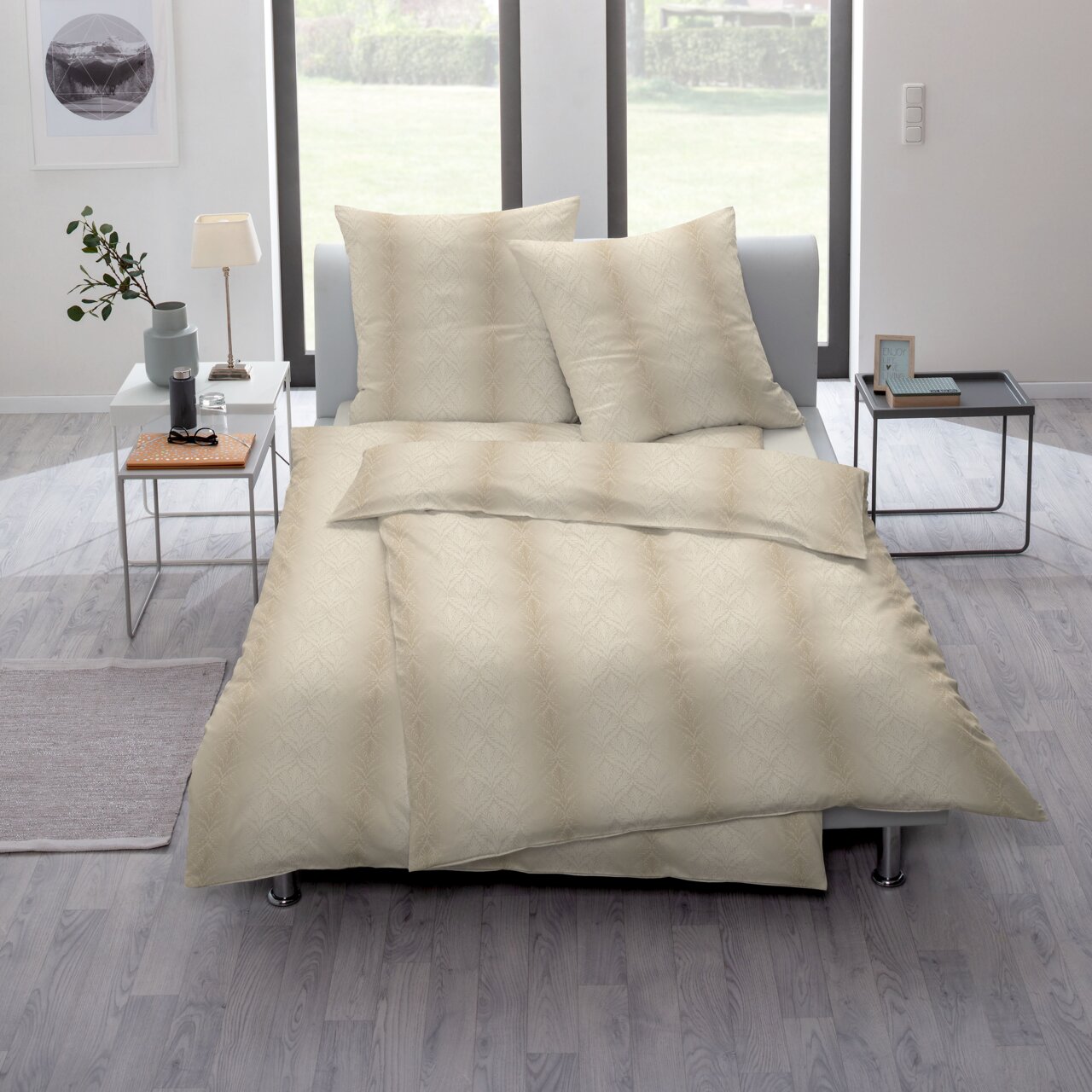 Elegante Bettwäsche in Beige mit dezentem Muster, auf einem modernen Bett in einem hellen Raum mit großen Fenstern präsentiert. Perspektive von schräg oben.