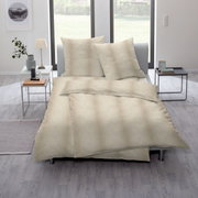 Elegante Bettwäsche in Beige mit dezentem Muster, auf einem modernen Bett in einem hellen Raum mit großen Fenstern präsentiert. Perspektive von schräg oben.