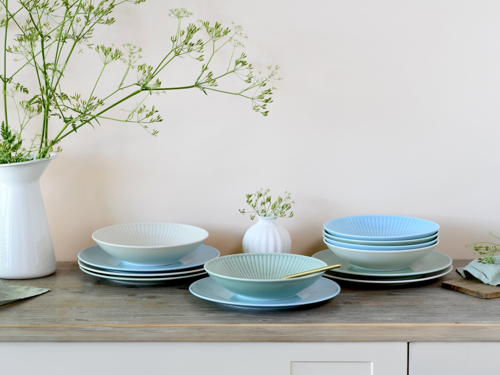 Creatable Tafelservice 12-tlg VALENCIA Pastellfarbenes Geschirr-Set mit geriffelten Schalen und Tellern auf Holztisch, daneben weiße Vasen mit grünen Zweigen; Perspektive: frontale Ansicht auf Tischhöhe