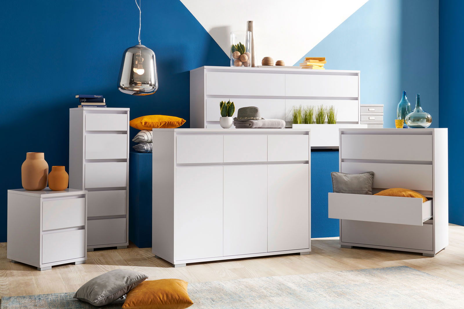 Carryhome Nachtkommode LINE Moderne weiße Möbelkollektion mit Hochkommode, Sideboard und Nachtkommode in einem stilvollen Raum mit blauer Wand, aus der Frontalperspektive.
