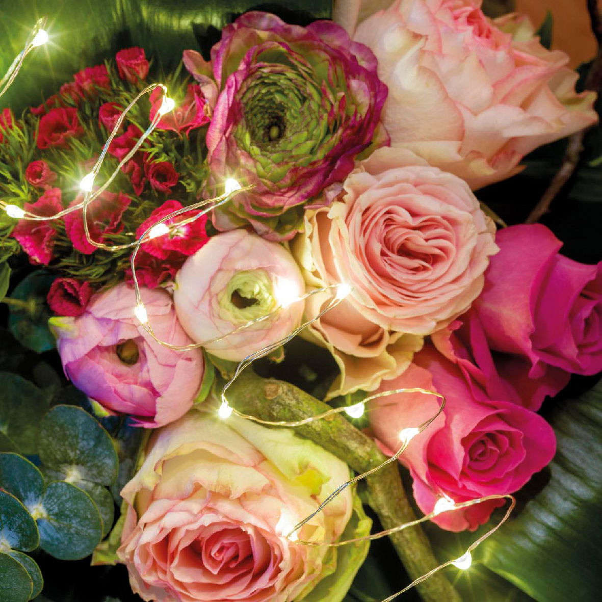 Nahaufnahme eines Blumenarrangements mit rosa und grünen Blüten, umgeben von leuchtenden LED-Lichtern.