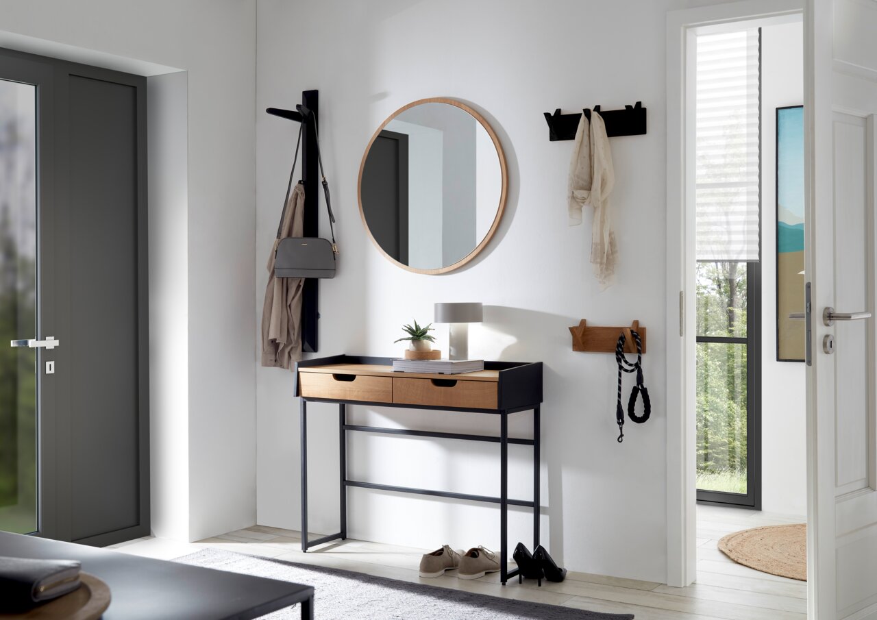 Linea Natura Garderobepaneel BANTRY Moderner Eingangsbereich mit runder Spiegel, Konsole mit zwei Schubladen und Hakenleisten an der Wand, seitliche Perspektive.