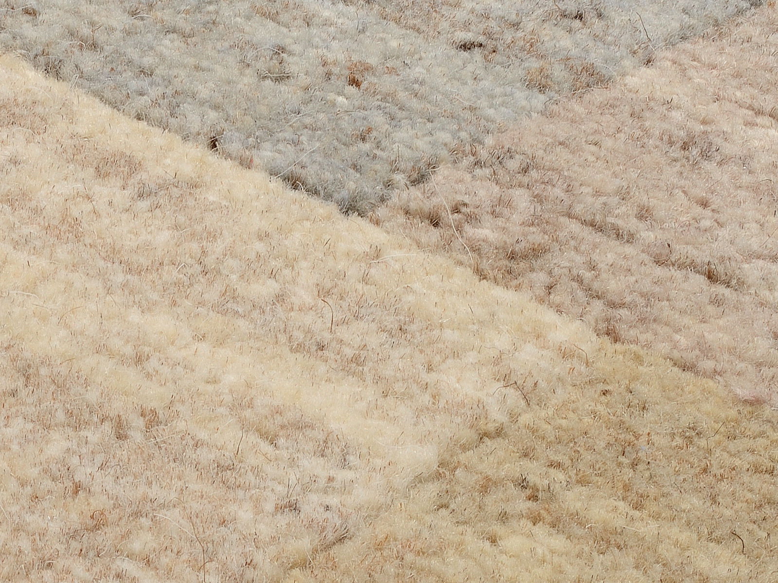 Nahaufnahme eines Wollteppichs mit verschiedenen Farbfeldern in Beige- und Grautönen, aus der Vogelperspektive aufgenommen.
