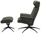 Seitliche Ansicht eines Einzelsessels mit Kopfstütze und passendem Fußhocker in dunkelgrünem Stoffbezug auf schwarzen Metallfüßen.