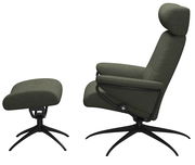 Seitliche Ansicht eines Einzelsessels mit Kopfstütze und passendem Fußhocker in dunkelgrünem Stoffbezug auf schwarzen Metallfüßen.