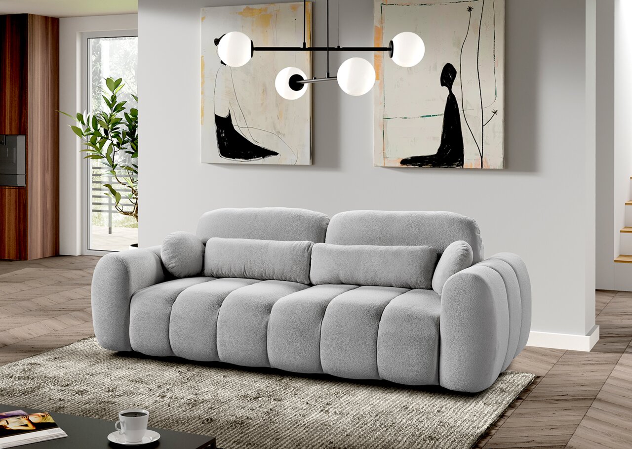 Graues Funktionssofa in einem modernen Wohnzimmer, frontal fotografiert, mit dekorativen Kissen und einem Teppich darunter.