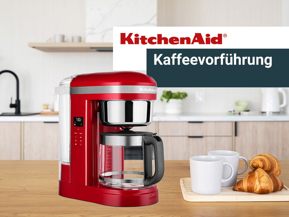 Rote KitchenAid-Kaffeemaschine in moderner Küche, daneben Tassen und Croissants auf einem Tablett, Hinweis auf Kaffeeführung