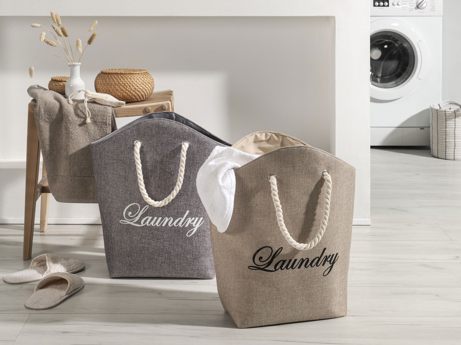 Zwei Wäschesäcke mit der Aufschrift 'Laundry' in einem modernen Waschraum, einer in Grau und einer in Beige, mit Seilgriffen, aus einer leicht seitlichen Perspektive fotografiert.