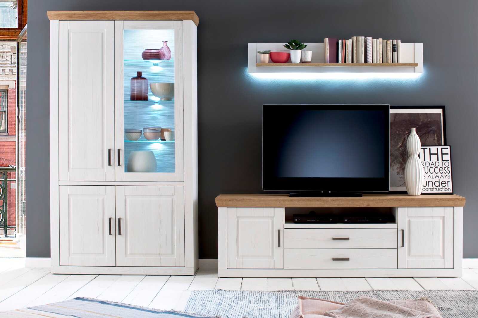 Wohnzimmermöbel-Set im Landhausstil: weiße Vitrine mit Glasfront und blauer LED-Beleuchtung sowie TV-Lowboard mit Holzoptik-Deckplatte, frontal aus Augenhöhe fotografiert