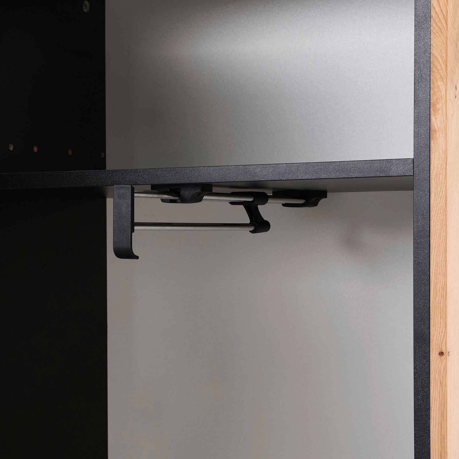 Innenansicht eines Garderobenschranks mit schwarzem Regalboden und Kleiderstange, seitliche Perspektive