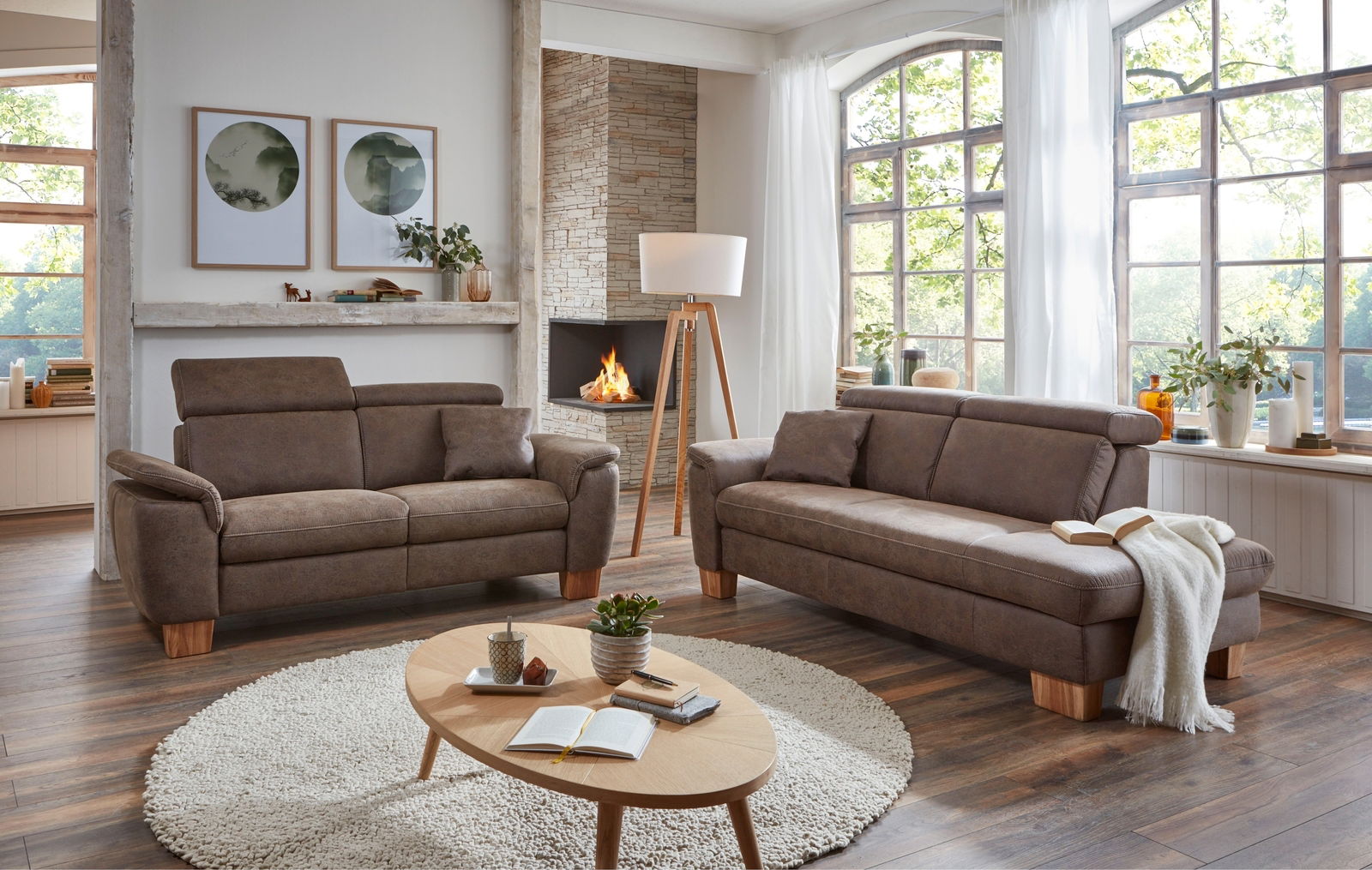 Gemütliches Wohnzimmer mit zwei braunen Sofas, einem runden Teppich und einem Holztisch, Blick auf die linke Seite der Recamiere.