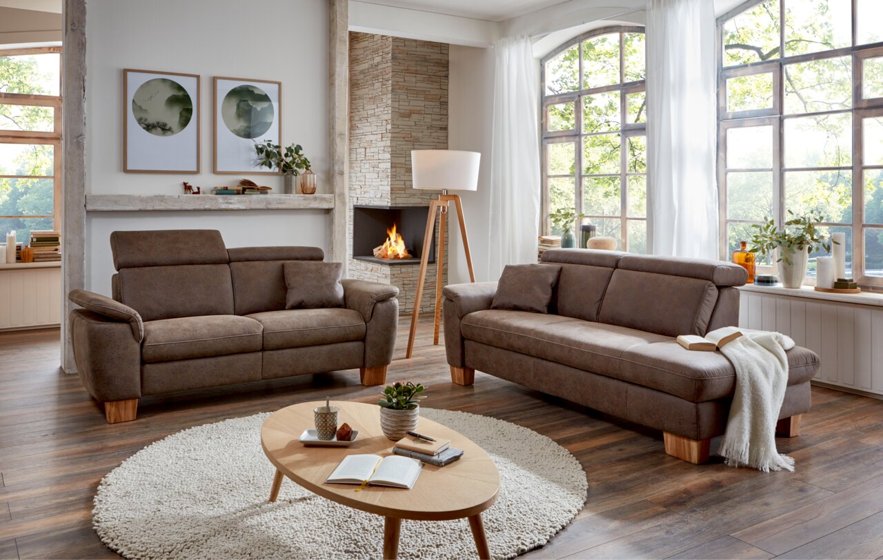 Gemütliches Wohnzimmer mit zwei braunen Sofas, einem runden Teppich und einem Holztisch, Blick auf die linke Seite der Recamiere.