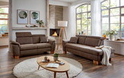 Gemütliches Wohnzimmer mit zwei braunen Sofas, einem runden Teppich und einem Holztisch, Blick auf die linke Seite der Recamiere.