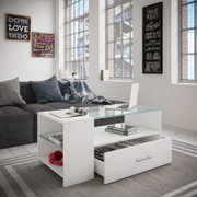Moderner weißer Couchtisch mit Glasplatte, offenem Fach und herausgezogener Schublade im Wohnzimmer neben grauem Sofa, frontale Perspektive leicht von links.