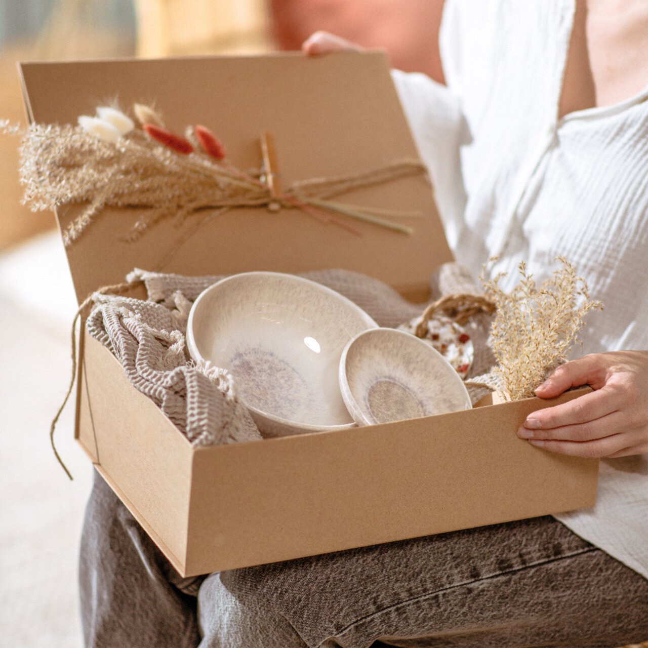 Like by Villeroy & Boch Dipschälchen PERLEMOR SAND Eine Person hält eine Geschenkbox mit zwei Dipschälchen in natürlichen Farben, dekoriert mit Trockenblumen, aus der Perspektive von oben betrachtet.