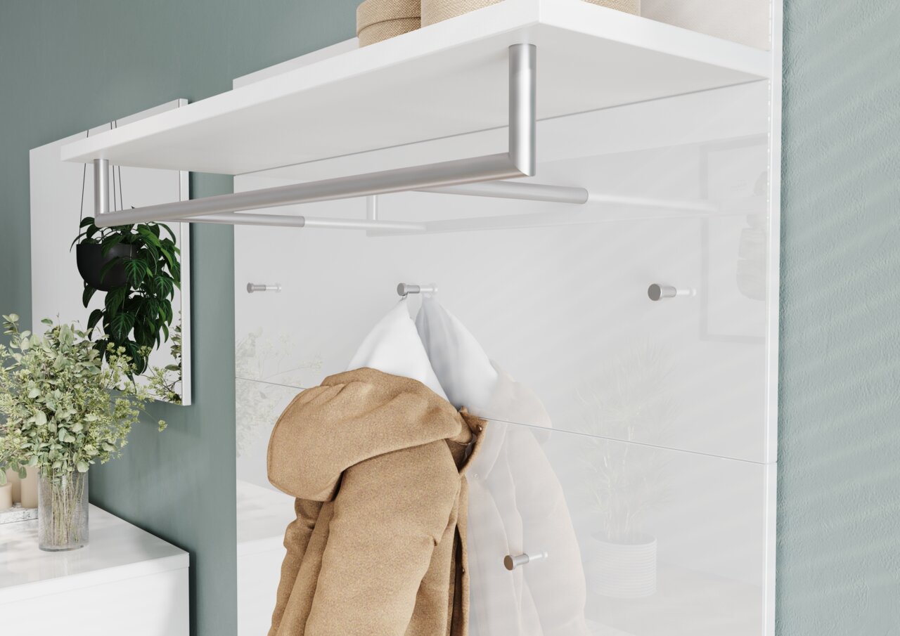 Garderobenpaneel mit weißem Regalbrett und silberner Kleiderstange, von der Seite betrachtet. Ein beiger Mantel hängt an einem Haken, umgeben von Pflanzen und Dekoration.