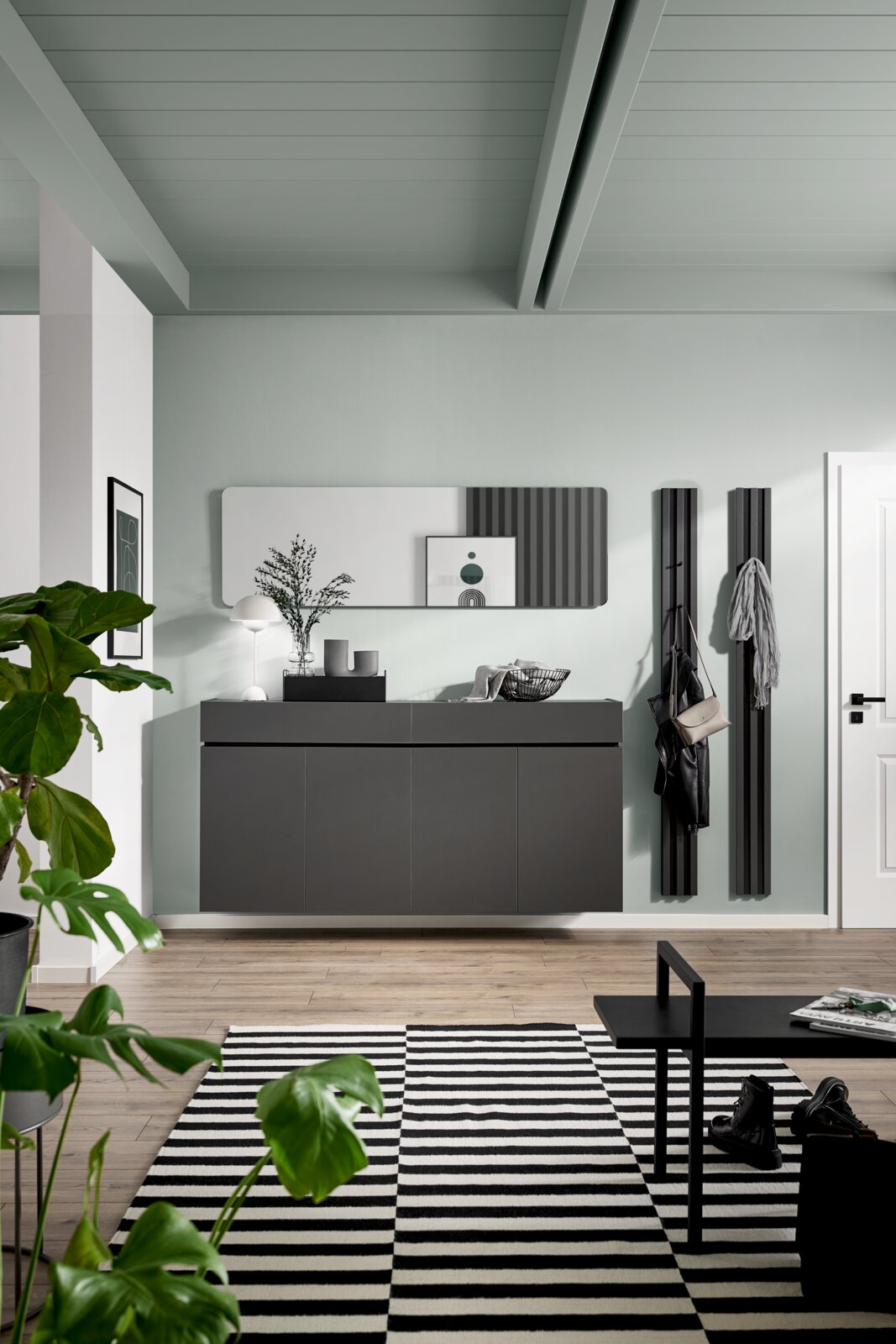 Voleo XXL-Schuhschrank UNIQUE Moderner, wandmontierter XXL-Schuhschrank in dunklem Design, frontal fotografiert, mit dekorativen Elementen und Pflanzen im Vordergrund.