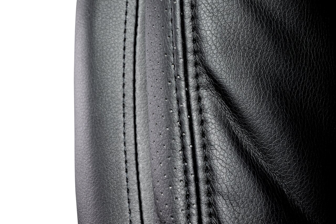 Close-up van de zwarte lederen bekleding van een directiestoel met zichtbare stiksels, gezien vanaf de zijkant