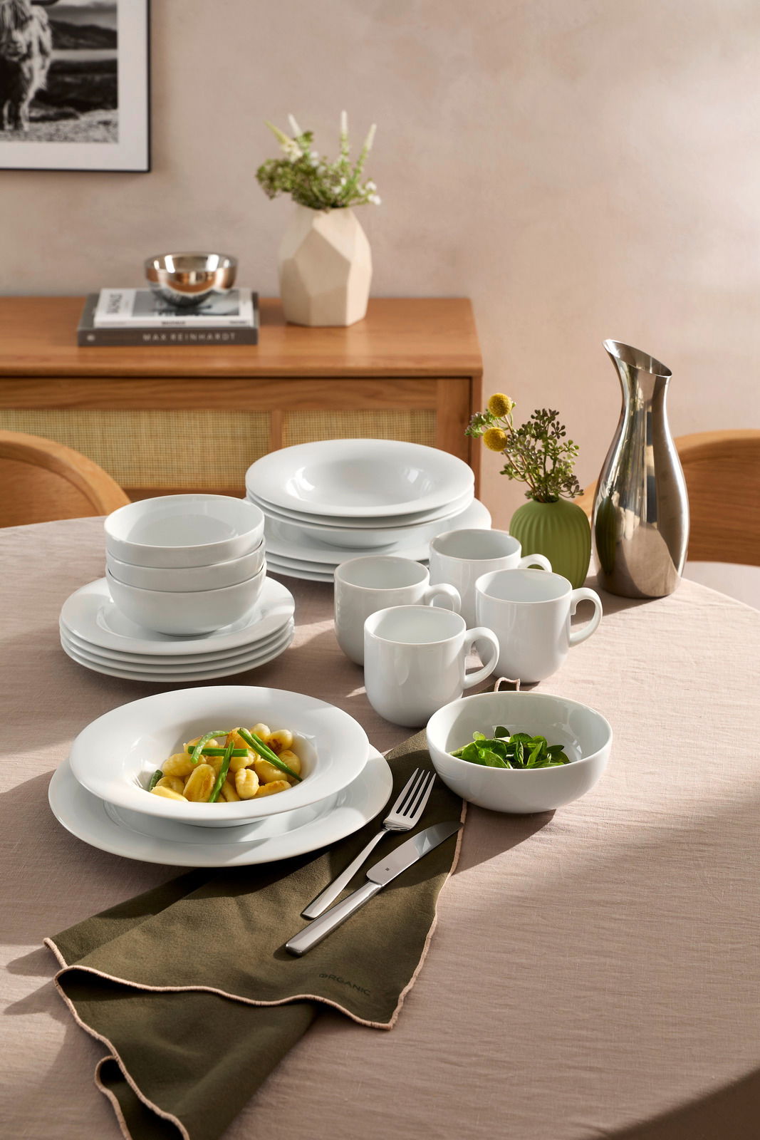 Elegantes weißes Kombiservice 20-tlg. auf einem gedeckten Tisch, mit Tellern, Schalen und Tassen, aus seitlicher Perspektive fotografiert.
