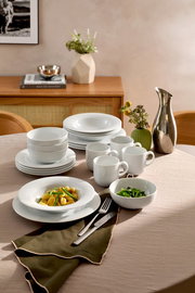 Elegantes weißes Kombiservice 20-tlg. auf einem gedeckten Tisch, mit Tellern, Schalen und Tassen, aus seitlicher Perspektive fotografiert.