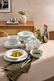 Elegantes weißes Kombiservice 20-tlg. auf einem gedeckten Tisch, mit Tellern, Schalen und Tassen, aus seitlicher Perspektive fotografiert.