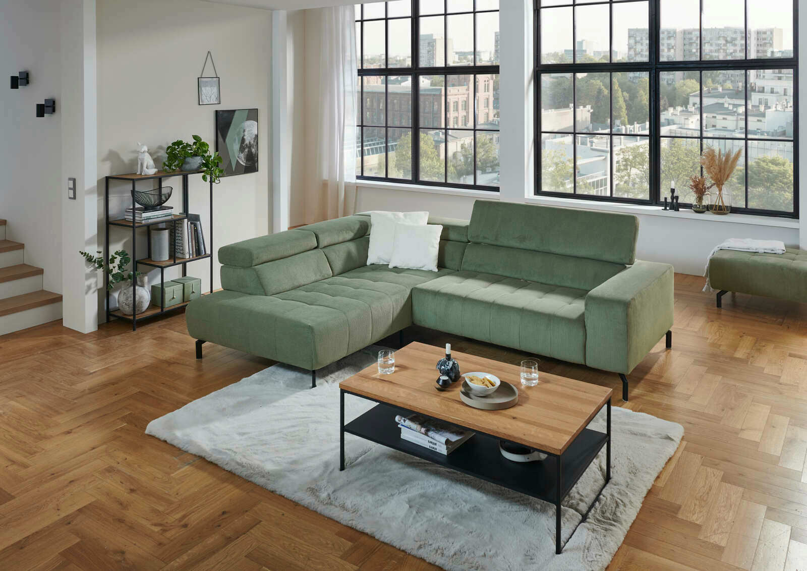 Grüne Eckgarnitur in modernem Wohnzimmer mit großen Fenstern, Holzboden und einem Couchtisch, Perspektive von vorne links.
