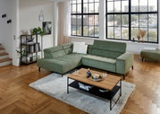 Grüne Eckgarnitur in modernem Wohnzimmer mit großen Fenstern, Holzboden und einem Couchtisch, Perspektive von vorne links.