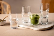 Set van transparante stapelbare glazen op een marmeren serveerplank, met één glas gevuld met groene iced matcha; zijaanzicht op tafelhoogte.
