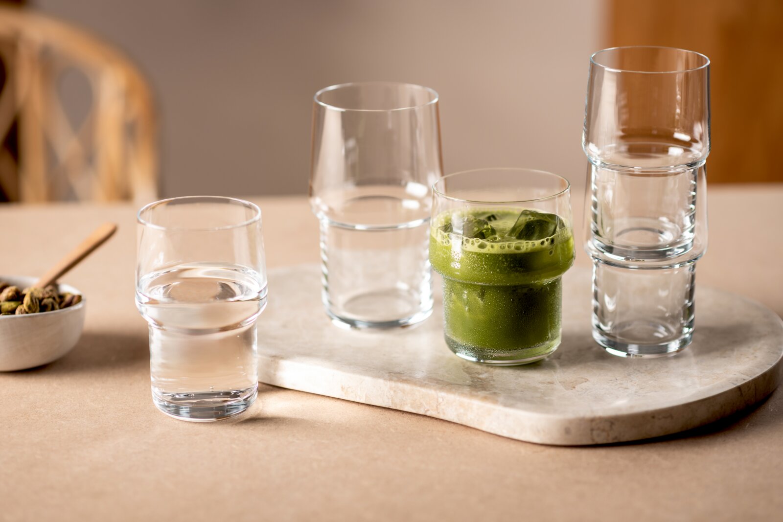 Set van transparante stapelbare glazen op een marmeren serveerplank, met één glas gevuld met groene iced matcha; zijaanzicht op tafelhoogte.