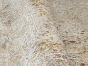 Nahaufnahme eines Designer Teppichs mit abstraktem Muster in Beige- und Goldtönen, perspektivisch von der Seite aufgenommen.