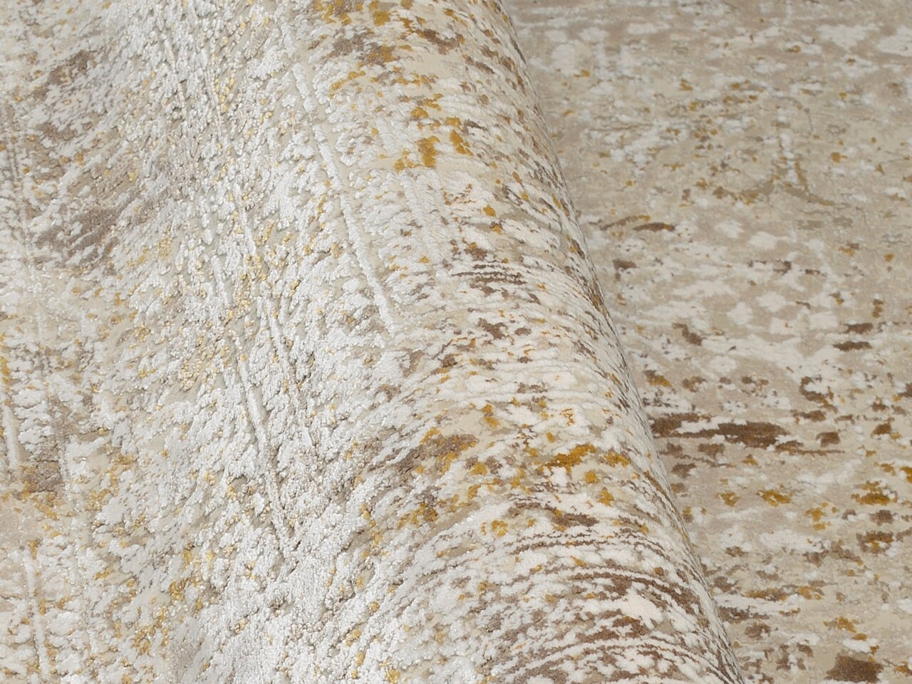 Nahaufnahme eines Designer Teppichs mit abstraktem Muster in Beige- und Goldtönen, perspektivisch von der Seite aufgenommen.