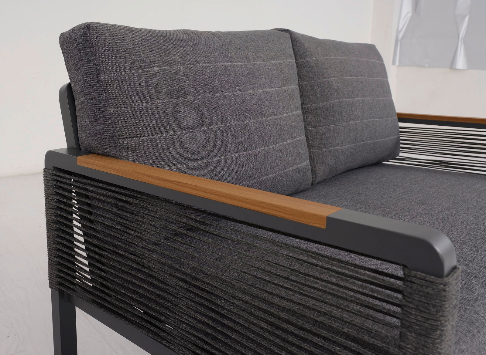 Nahaufnahme einer modernen, zweisitzigen Sitzbank mit grauen Polstern und Armlehnen aus Holz und Metall. Die Perspektive zeigt die rechte Seite der Bank.