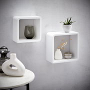 Zwei weiße, quadratische Wandregale aus Holz, an einer grauen Wand montiert, mit dekorativen Vasen und Pflanzen, seitliche Perspektive.