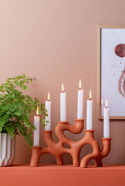 Kerzenhalter SWIRLS Large in organischer Form mit sieben brennenden Kerzen, seitliche Perspektive, auf einem Regal neben einer Pflanze und einem Bild.